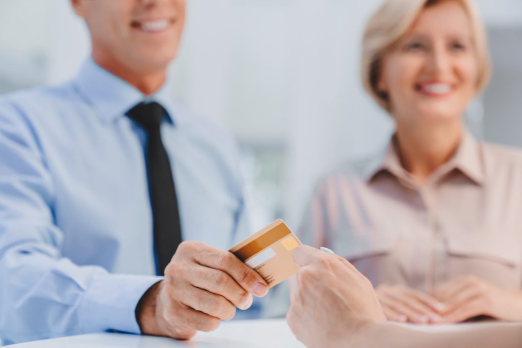 Close up cropped shot of adult couple paying at hotel, clinic, shop with credit card